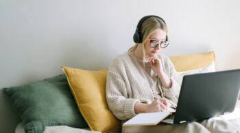 Photo of a lady working on her laptop and writing in a notebook at home