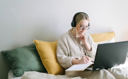 Photo of a lady working on her laptop and writing in a notebook at home