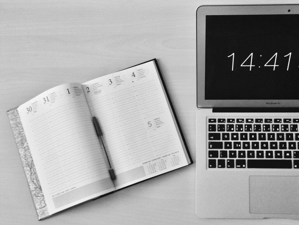 An open work diary next to a laptop displaying the time