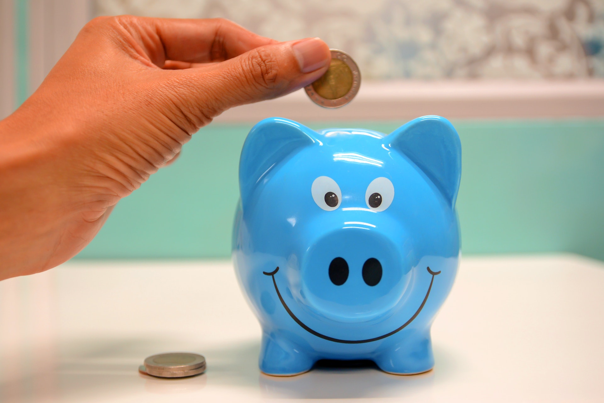 A hand putting a coin in a smiling blue piggy bank