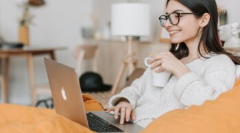 Lady typing on her laptop with one hand and holding a mug in the other hand