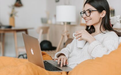 Lady typing on her laptop with one hand and holding a mug in the other hand