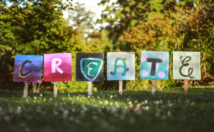 Wooden boards that have been staked into the grass, colourfully painted with letters to spell CREATE