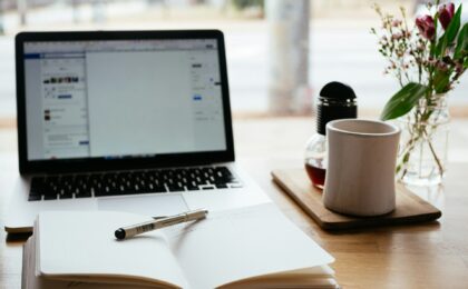 A laptop with a pen and notebook in front of it and a mug to the side