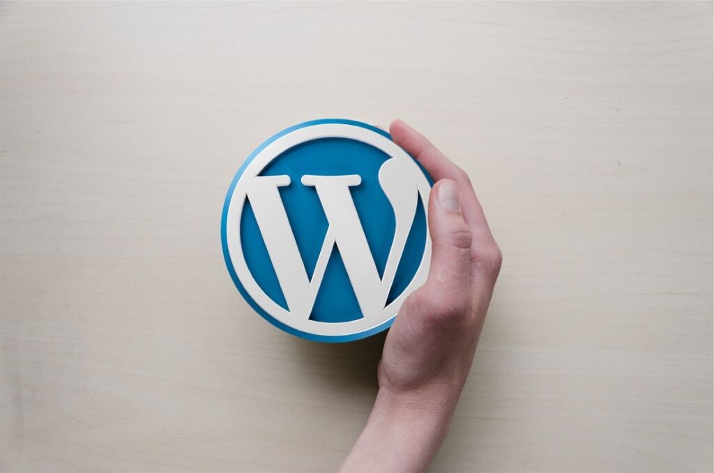 A raised WordPress logo with a hand curved around the right-hand side of it.